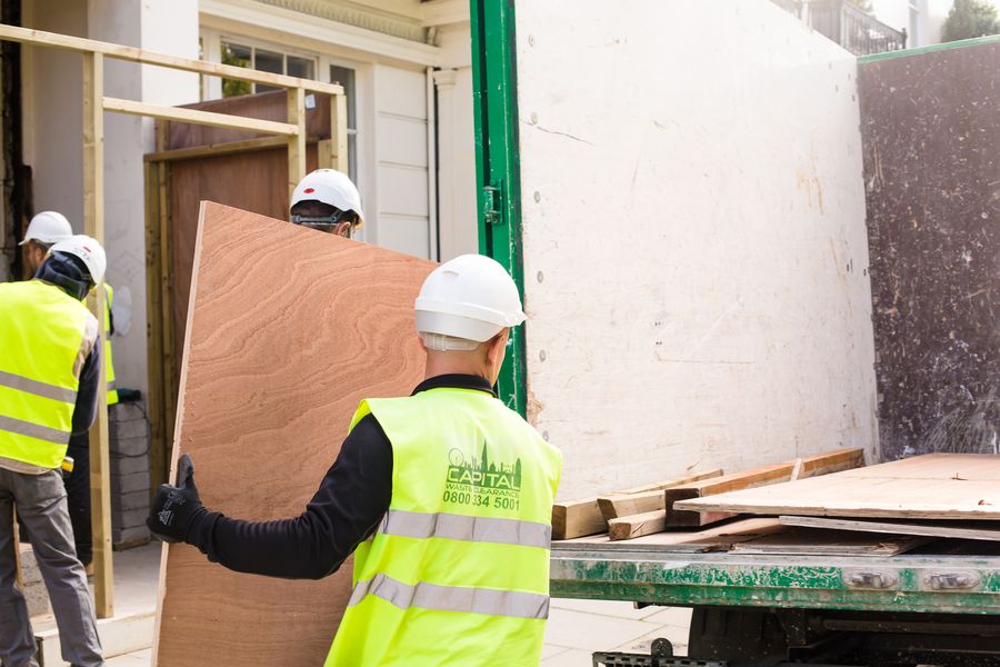 Capital Waste Clearance workers carrying large boards into truck on a London street